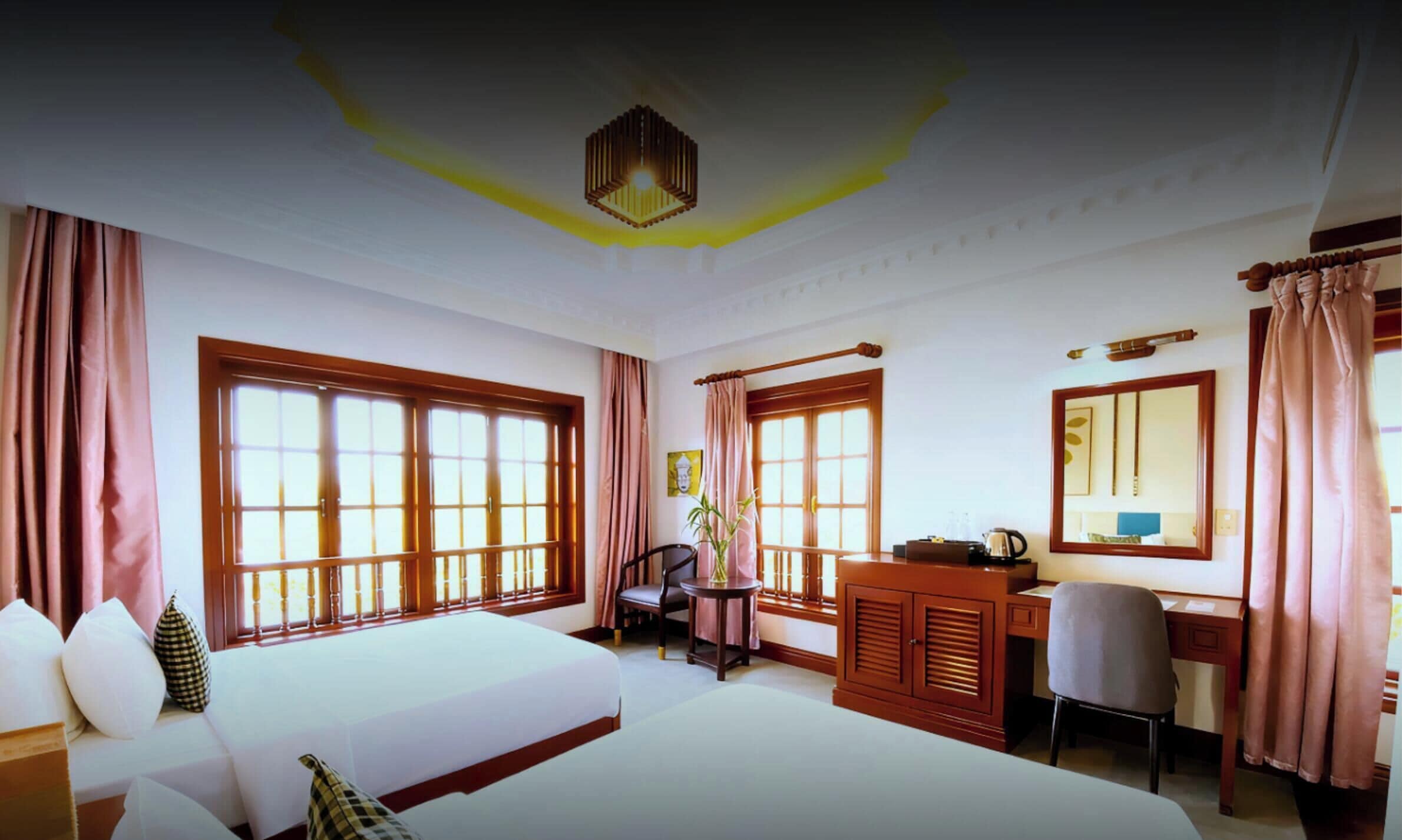 A hotel room with two beds, a desk, a chair, and large windows.