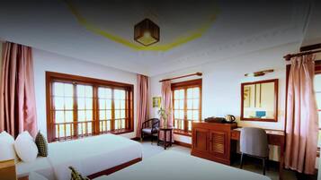 A hotel room with two beds, a desk, a chair, and large windows.