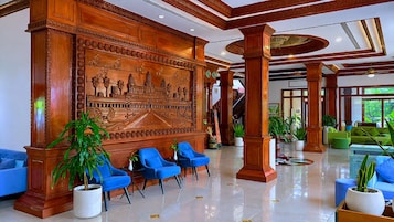 Um hall com um grande painel de madeira, cadeiras azuis e plantas em vasos.