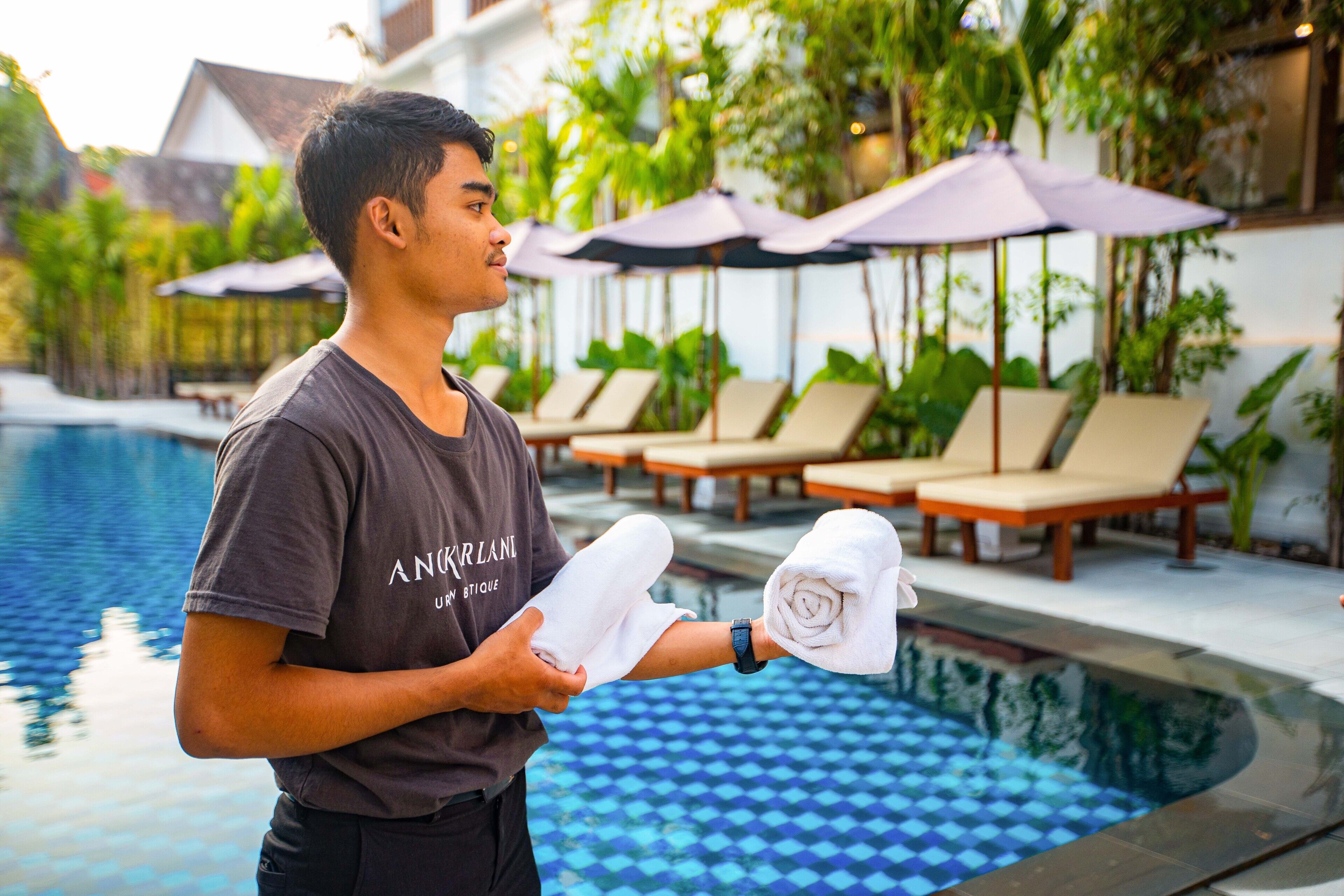 A man holding towels by a pool with lounge chairs and umbrellas in the background.