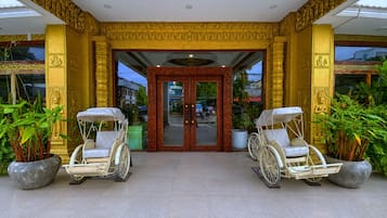 A building entrance with ornate golden pillars, a glass door, and two rickshaws on either side.