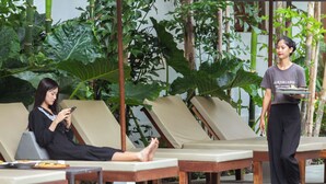Un área de descanso con sillones de madera y una persona sosteniendo una bandeja.