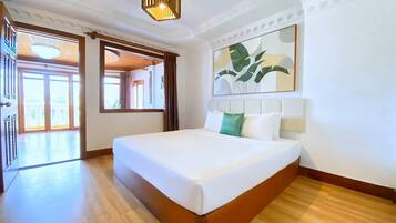 A hotel room with a large bed, wooden flooring, a ceiling light fixture, and a large window with curtains.