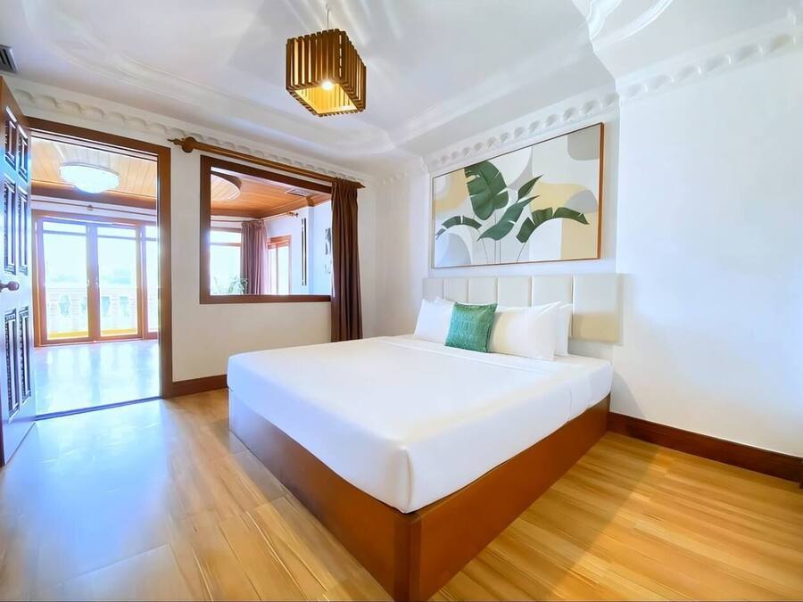 A hotel room with a large bed, wooden flooring, a ceiling light fixture, and a large window with curtains.