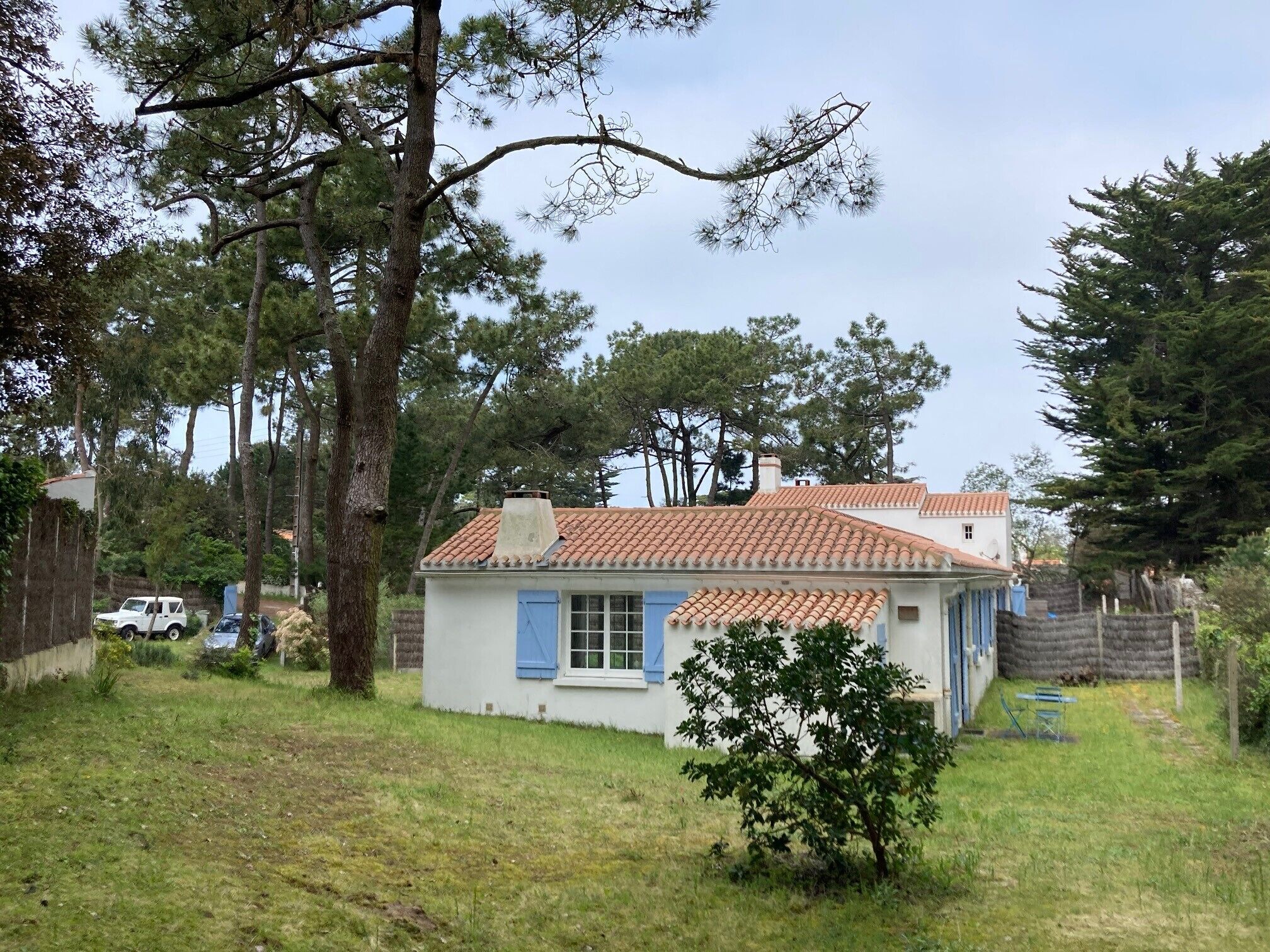 A small house with a tiled roof, surrounded by trees and a grassy yard.