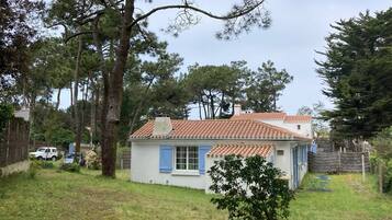 A small house with a tiled roof, surrounded by trees and a grassy yard.