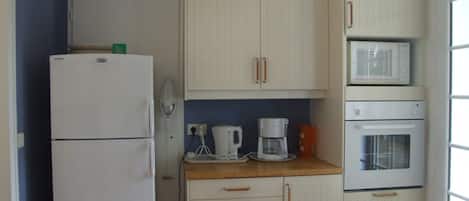 Cocina compacta equipada con refrigerador, microondas, cafetera y horno.