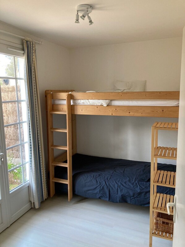 Habitación con literas, una escalera de madera, un estante pequeño y una ventana con cortinas.