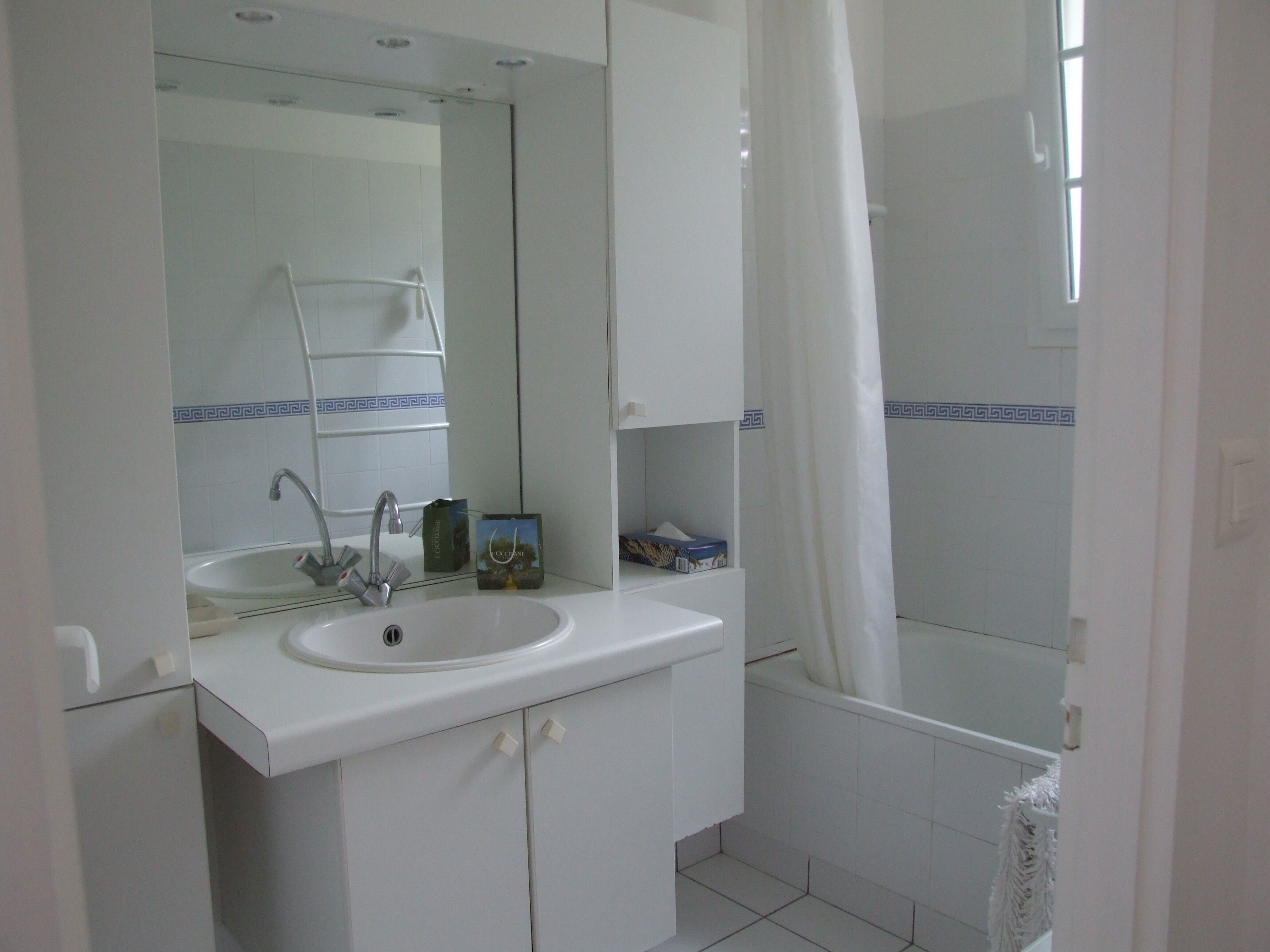 A bathroom with a white sink, mirror, and bathtub. There is a towel rack above the sink and a shower curtain partially drawn.