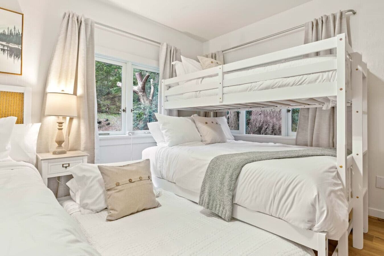 A bedroom with bunk beds, a bedside table with a lamp, and a window with a view of greenery.