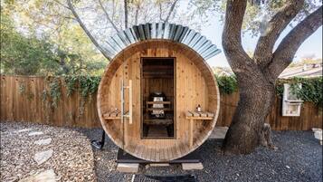 Relax in a secluded garden setting, surrounded by a large tree, with a rustic sauna or hot tub.