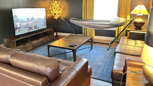 Ein Wohnzimmer mit Fernseher, einer Hängematte, Ledersofas, einem Couchtisch und einer Lampe.