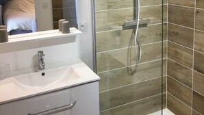A modern bathroom with a glass-enclosed shower, a white sink, and a mirror above it. - Gîte 12 Personnes (Brem-sur-Mer)