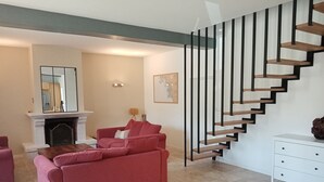 A modern living room with a red sofa, a fireplace, and a staircase with wooden steps and black railings. - Gîte 12 Personnes (Brem-sur-Mer)