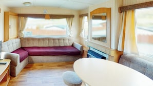 A cozy RV interior with a sofa, a dining table, and a fireplace. - Comfortable caravan with one double and two twin. (Fishguard, Pembrokeshire)