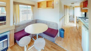 A compact RV interior with a seating area, a small table, a kitchenette, and a television. - Comfortable caravan with one double and two twin. (Fishguard, Pembrokeshire)