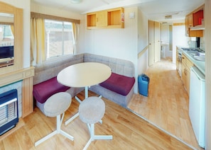 A compact RV interior with a seating area, a small table, a kitchenette, and a television. - Comfortable caravan with one double and two twin. (Fishguard, Pembrokeshire)