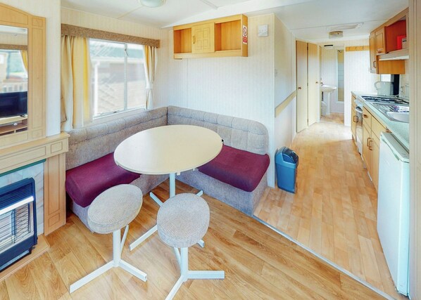 A compact RV interior with a seating area, a small table, a kitchenette, and a television. - Comfortable caravan with one double and two twin. (Fishguard, Pembrokeshire)