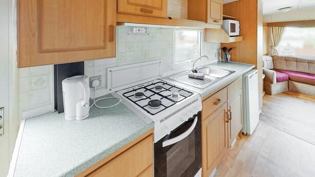 A compact kitchen with a gas stove, sink, and microwave. - Comfortable caravan with one double and two twin. (Fishguard, Pembrokeshire)