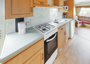 A compact kitchen with a gas stove, sink, and microwave. - Comfortable caravan with one double and two twin. (Fishguard, Pembrokeshire)