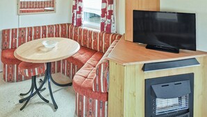 A cozy RV interior with a sectional sofa, a round table, a television, and a wood stove. - Comfortable caravan with one double and two twin. (Fishguard, Pembrokeshire)
