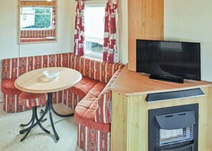 A cozy RV interior with a sectional sofa, a round table, a television, and a wood stove. - Comfortable caravan with one double and two twin. (Fishguard, Pembrokeshire)