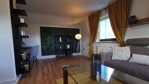 Un salon moderne avec un canapé, une table basse en verre, une bibliothèque et une plante fixée au mur.