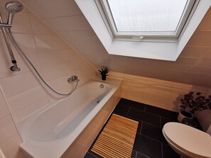 Une salle de bain moderne avec un puits de lumière, une baignoire, des toilettes et une petite plante en pot.