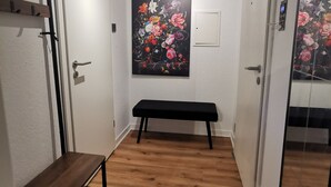Un couloir avec un banc en bois, un luminaire au plafond, un tableau accroché au mur et une porte dotée d’une poignée.