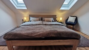 Une chambre avec un lit en bois, deux tables de chevet avec des lampes, une chaise et des fenêtres de toit.