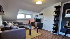 Un salon moderne avec un canapé, une table basse en verre, un téléviseur et une bibliothèque.