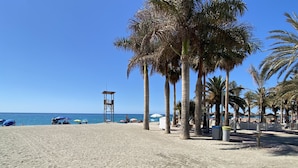 Une plage bordée de palmiers, avec des parasols et une tour de surveillance pour les sauveteurs.