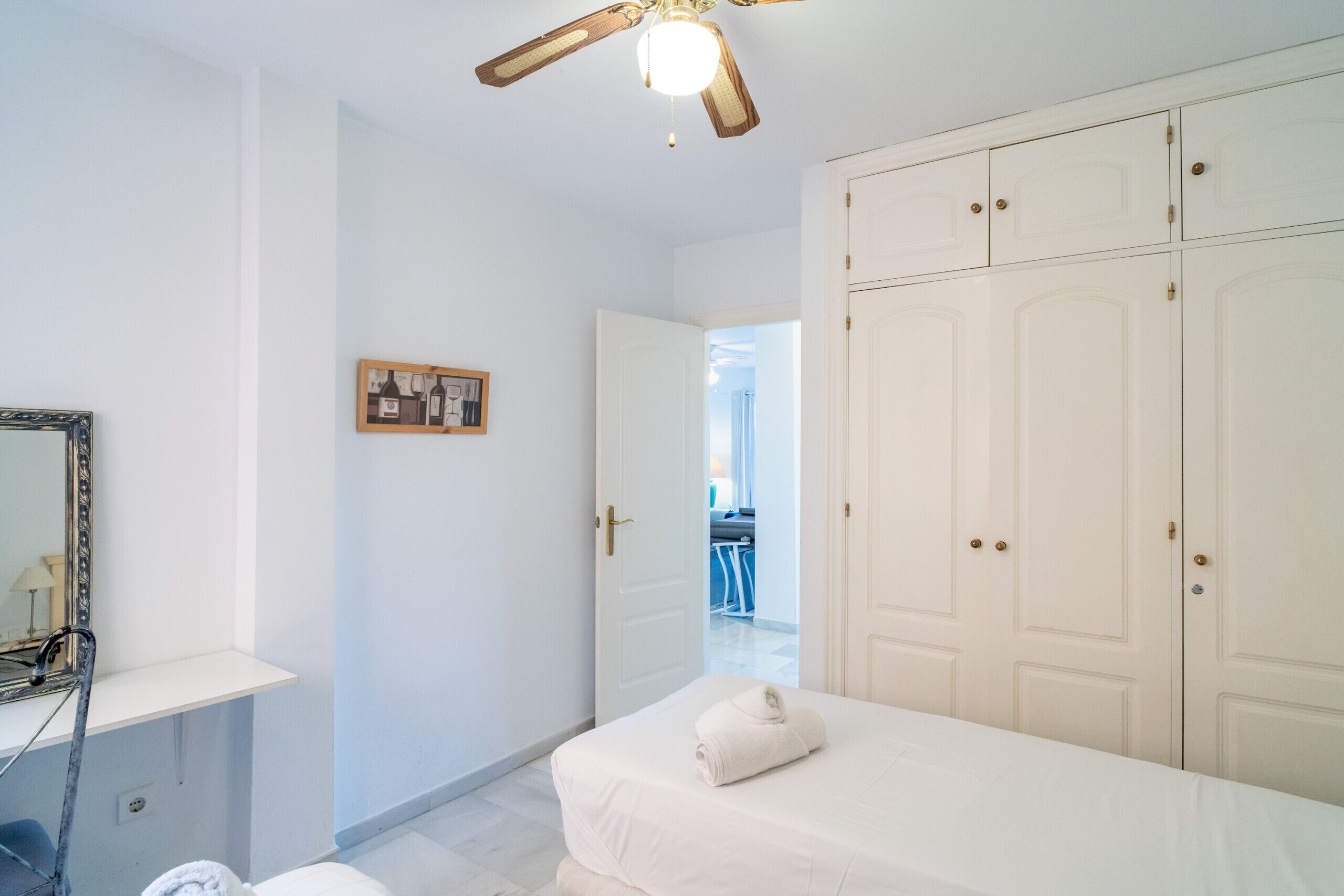 Une chambre à coucher comprenant un lit, un ventilateur de plafond, une armoire et une porte donnant sur une autre pièce.