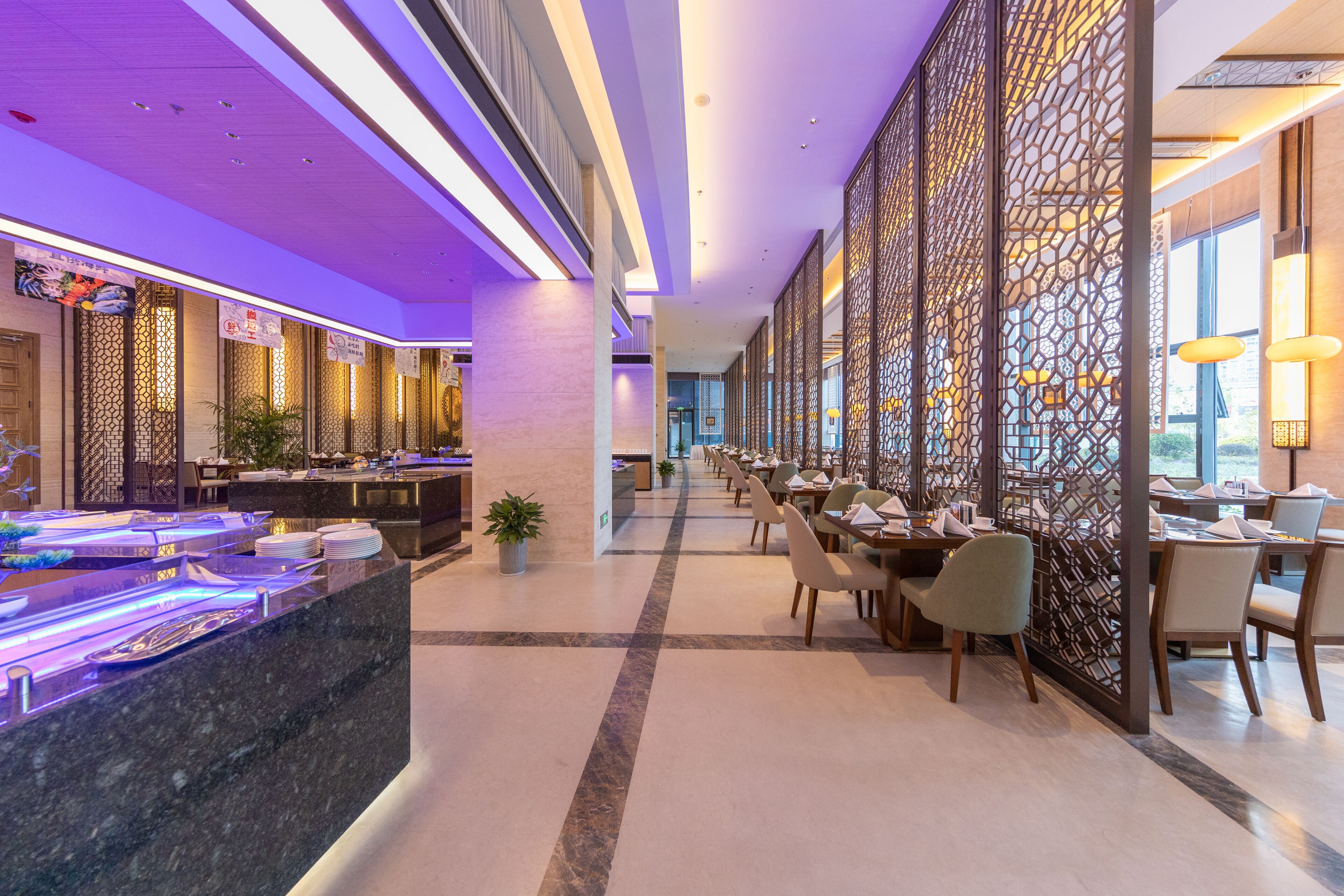 A modern hotel lobby with a reception desk, seating area, decorative screens, and a view of the city.