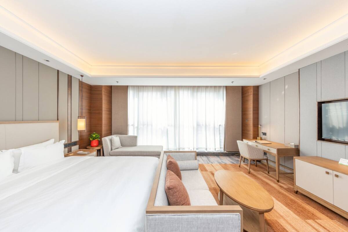 Ein modernes Hotelzimmer mit einem großen Bett, einer Couch, einem Schreibtisch und einem Fernseher.
