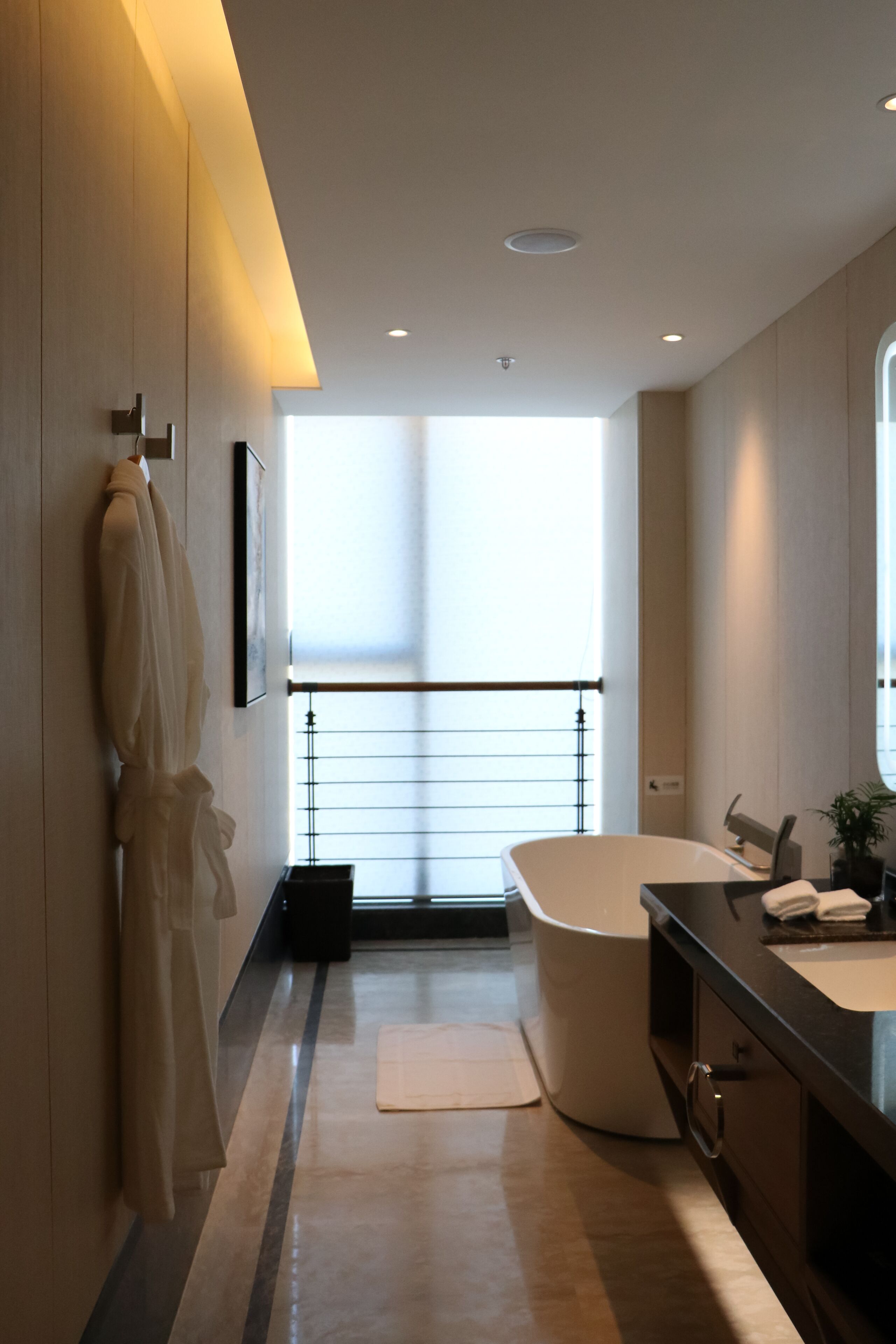 Ein modernes Badezimmer mit einer großen Badewanne, einem Waschtisch mit Spiegel und einem Bademantel, der an der Wand hängt.