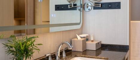 Een moderne badkamer met een wastafel, twee spiegels, een zeepdispenser en een plant in pot.