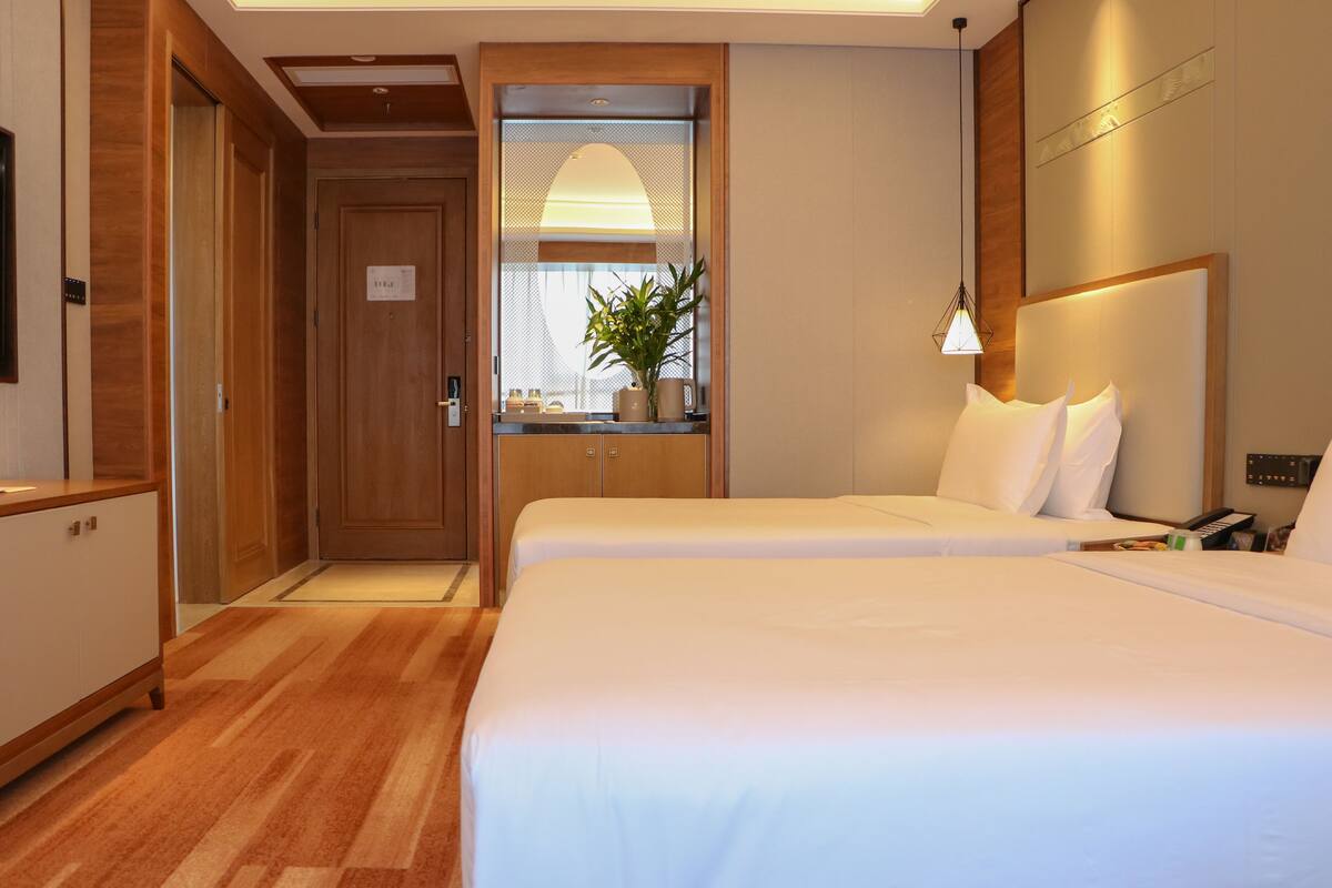 Ein Hotelzimmer mit einem großen Bett, einem Holzschrank, einem kleinen Tisch mit Pflanze und einem Nachttisch mit Lampe.