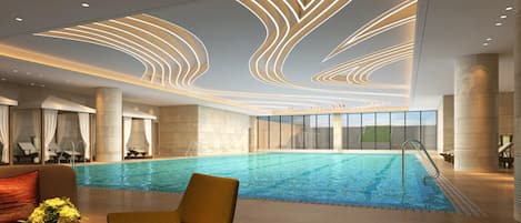 A modern indoor swimming pool with a sleek ceiling design, a clear view of the outdoors, and a comfortable seating area with a vase of flowers.