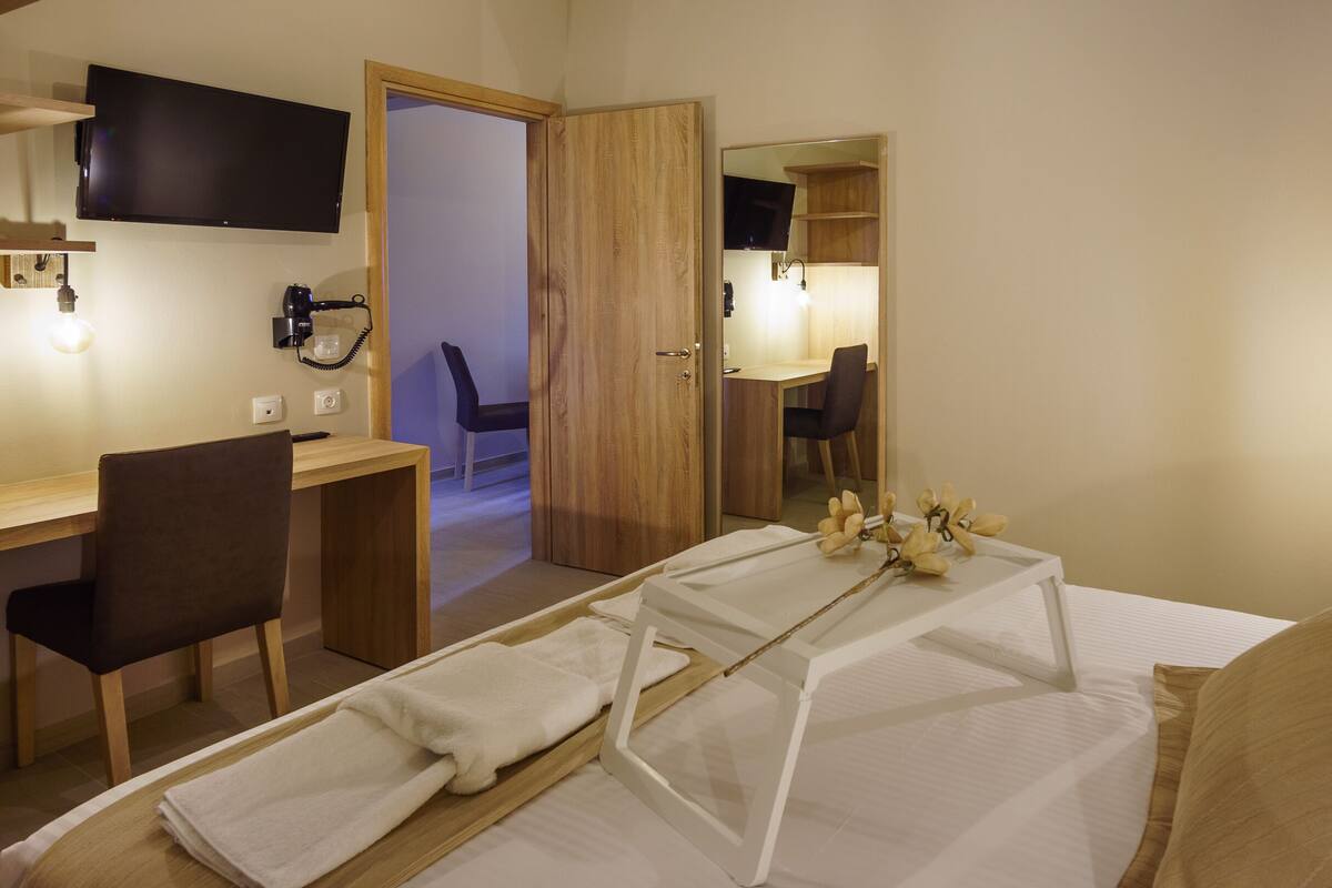 A hotel room with a bed, a desk, a chair, a TV, and a mirror.
