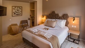 Un dormitorio ordenado con una cama grande, una mesita de noche, una silla y un televisor montado en la pared.