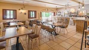 Un restaurante con varias mesas y sillas, una zona de bar con mostrador de ladrillo y vistas a zonas verdes al exterior.