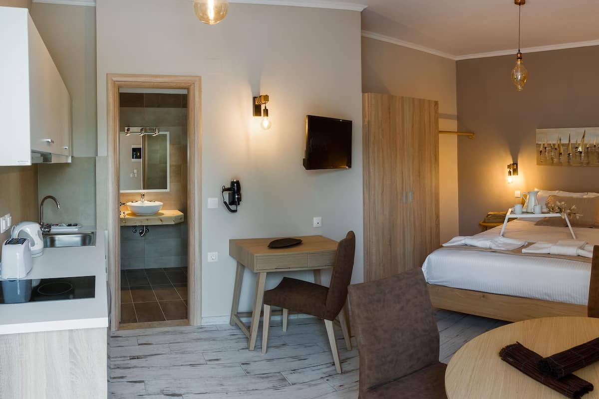 A hotel room with a bed, a desk, a chair, a round table, a TV, a mirror, a sink, and a shower.