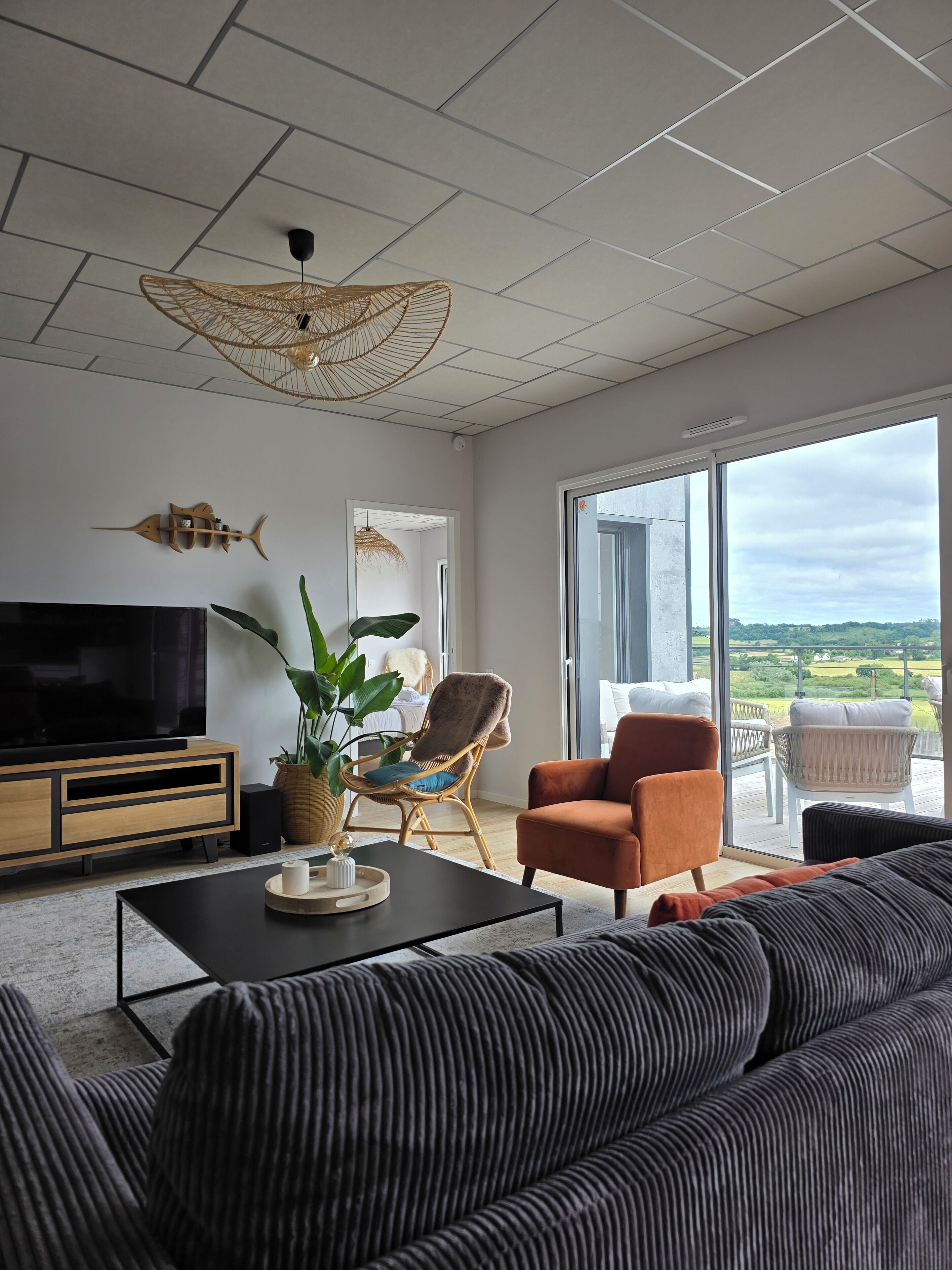 Ein modernes Wohnzimmer mit einem großen Flachbildfernseher, einer Couch, einem Couchtisch und einem Balkon mit Blick auf die Landschaft.