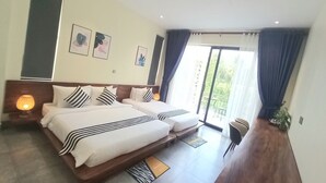 A hotel room with two beds, a nightstand with a lamp, a dining table, and a view of the outdoors through a large window. - Kampot Tropical Village (Kampot)