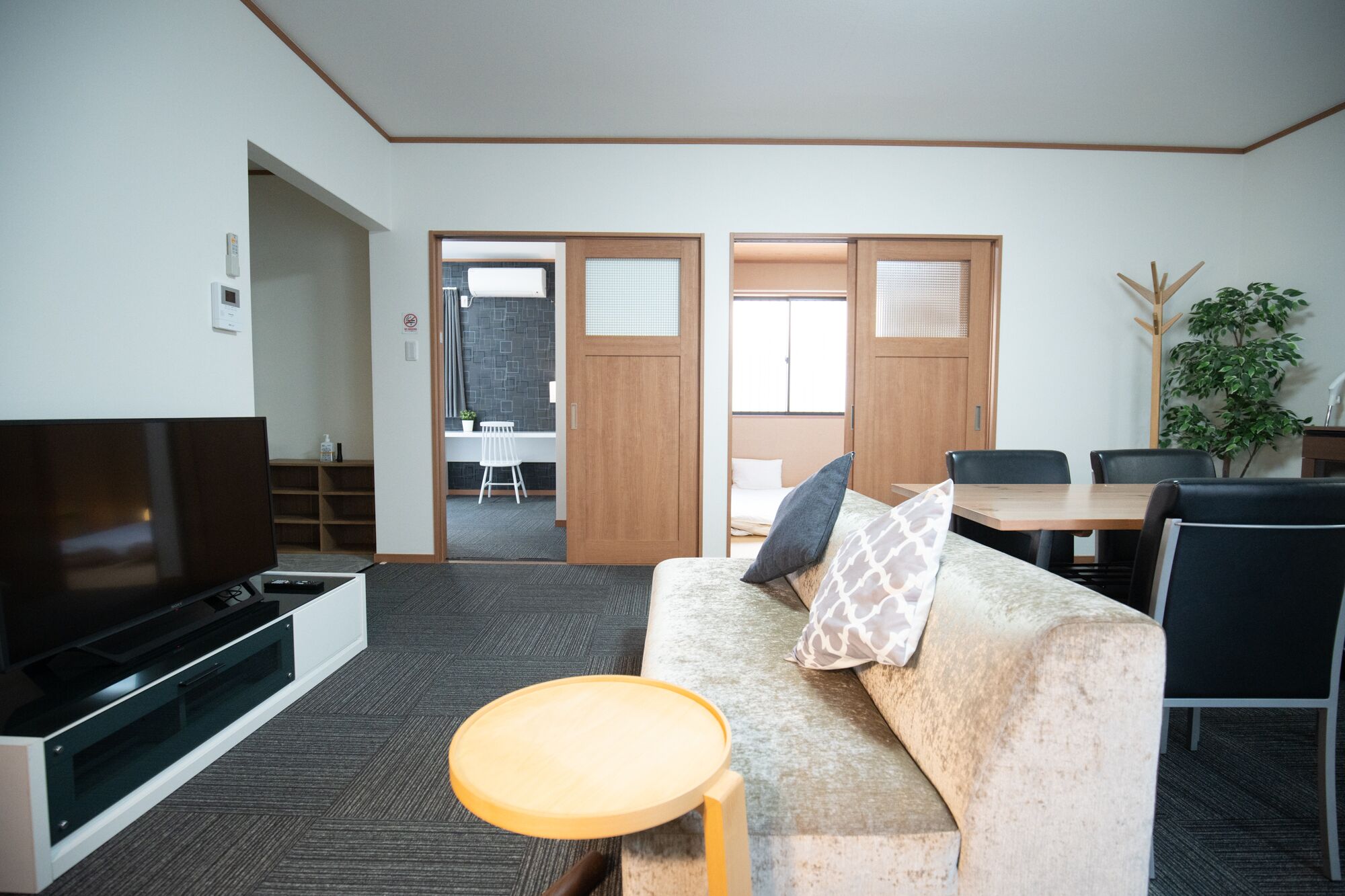 A modern hotel room with a sofa, a small round table, a TV, and a dining area with chairs and a table.