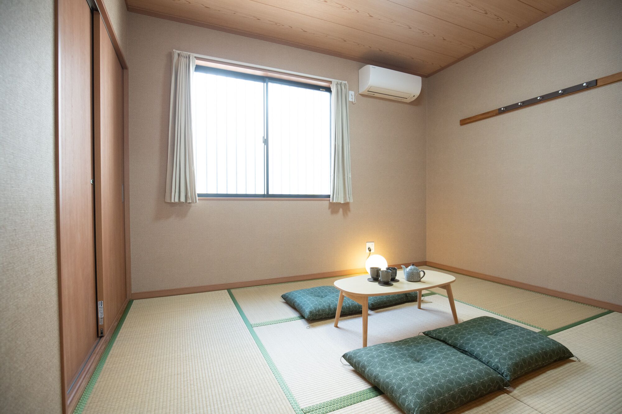 A traditional Japanese room with tatami flooring, a shoji screen, a small table with a tea set, and a futon bed.