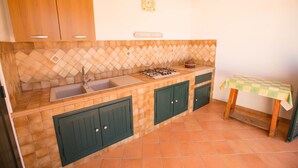 A kitchen with a tiled backsplash, wooden cabinets, a sink, a stove, and a small table with a checkered tablecloth. - Flower Apartment (Cefalù)