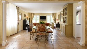 Un'ampia sala da pranzo con un tavolo rotondo e poltrone decorate, un pianoforte e un televisore a parete.