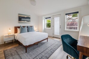 A bedroom with a bed, nightstands, a desk, a chair, a painting, and a view through a door. - Modern 3BR in the Heart of Ballard | Private Patio (Seattle)